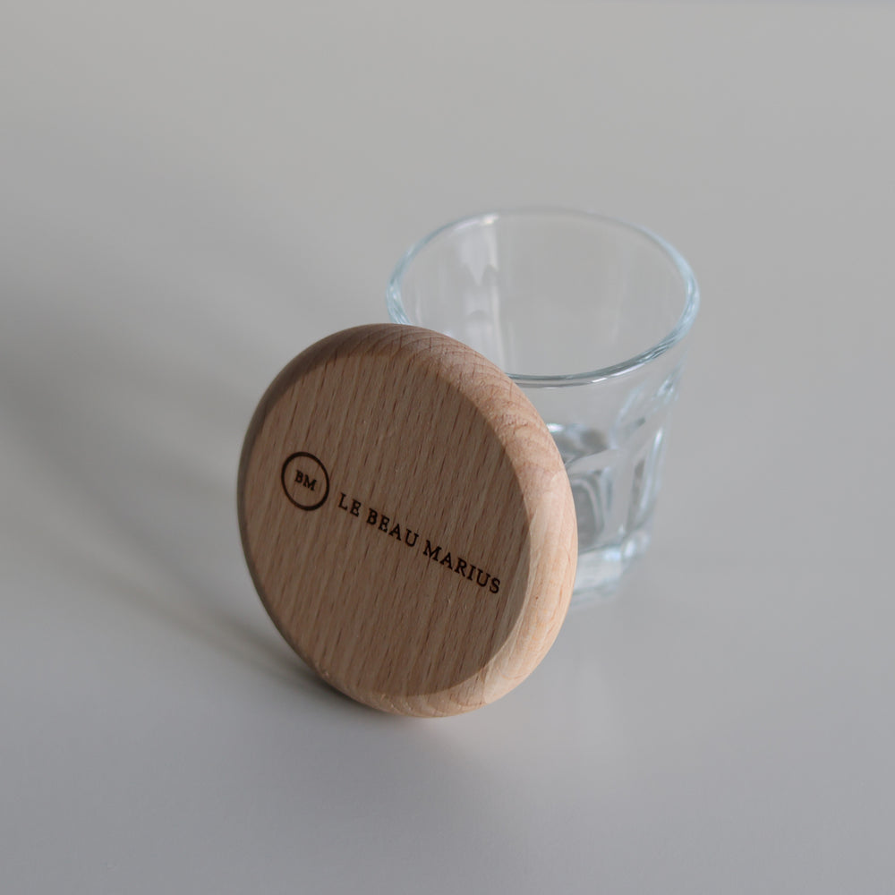 Décapsuleur en hêtre Le Beau Marius appuyé contre un verre, vue de côté